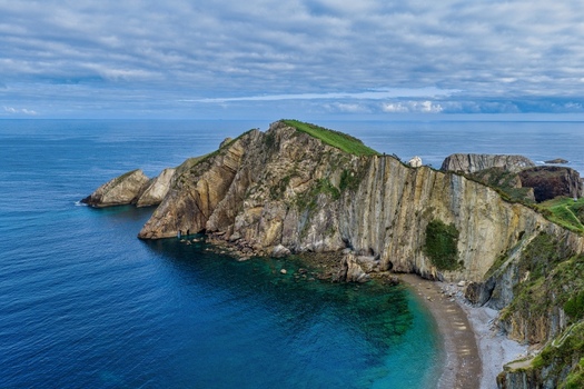 Aerial view of the dramatic cliffs and turquoise waters of Silence Beach Viewpoint with its rugged coastline and rocky formations under a cloudy sky in Cudillero Asturias Spain.