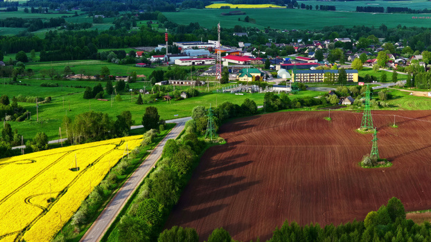 Aerial view of a rural landscape with a yellow rapeseed field a plowed brown field power lines and a small village with buildings and green trees in the background in Latvia. Aerial view of a rural landscape with a yellow rapeseed field a plowed brown field power lines and a small village with buildings and green trees in the background in Latvia.