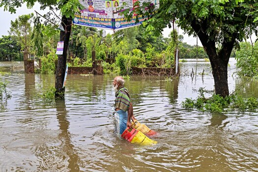 Banshkhali Upazila Chittagong Division Bangladesh 10 July 2026 View of an elderly man wading through floodwaters while carrying two gas cylinders in a submerged area. Banshkhali Upazila Chittagong Division Bangladesh 10 July 2026 View of an elderly man wading through floodwaters while carrying two gas cylinders in a submerged area.