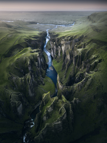 Aerial view of Fjadrargljufur Canyon featuring steep mossy cliffs and a winding river under a soft twilight sky Iceland.