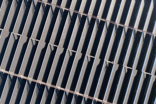 Aerial view of a large warehouse roof with repeating geometric patterns and long shadows cast across the industrial metal structure in Warsaw Masovian Voivodeship Poland.