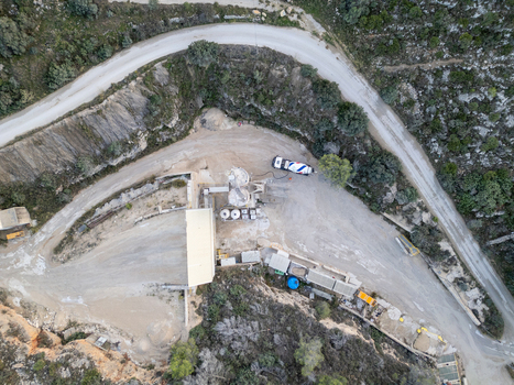 Aerial view of an industrial quarry site with machinery and gravel piles surrounded by winding roads and rocky terrain in Teulada Valencian Community Spain.