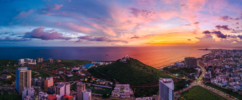 Aerial view of Deux Mamelles lighthouse on a green hill overlooking the Atlantic Ocean and city buildings under a vibrant sunset sky in Dakar Dakar Region Senegal.