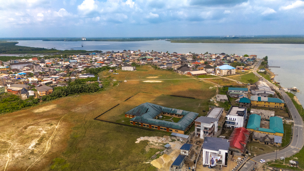 Aerial view of a coastal town with residential buildings a large school complex and a winding road along the riverbank in Rivers Nigeria.
