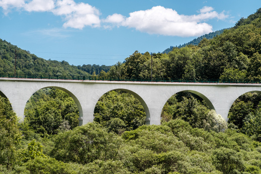 View of the arched railway viaduct surrounded by lush green forest and trees under a blue sky in Savnik Savnik Municipality Montenegro. View of the arched railway viaduct surrounded by lush green forest and trees under a blue sky in Savnik Savnik Municipality Montenegro.
