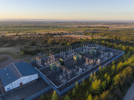 Aerial view of Eaglesham Moor electrical substation with power lines and transformers surrounded by green trees under a golden sunset sky Kilmarnock Scotland United Kingdom.