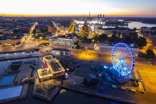 Aerial view of Allas Pool and the illuminated SkyWheel Helsinki with the Uspenski Cathedral glowing in the background during the twilight hour in Helsinki Uusimaa Finland.