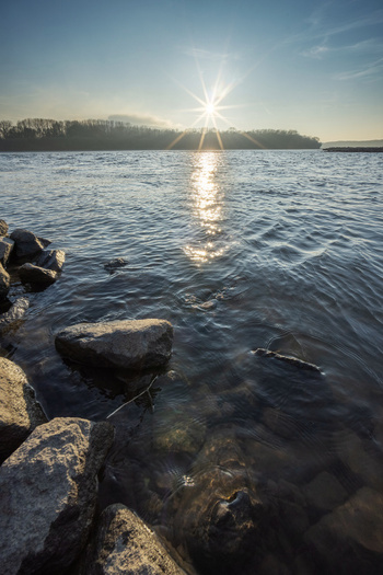 View of the Danube river near Devin at sunset with a sun starburst over the water and rocky shore Bratislava IV Bratislava Region Slovakia. View of the Danube river near Devin at sunset with a sun starburst over the water and rocky shore Bratislava IV Bratislava Region Slovakia.