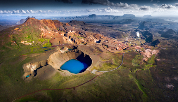 Aerial view of the bright blue Viti crater lake surrounded by rugged volcanic mountains and geothermal steam in the Krafla area Iceland.