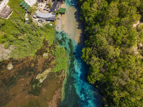 Aerial view of the Blue Eye natural spring with its vibrant turquoise water surrounded by lush green forest and small structures in Finiq Vlore County Albania. Aerial view of the Blue Eye natural spring with its vibrant turquoise water surrounded by lush green forest and small structures in Finiq Vlore County Albania.