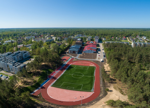 Aerial view of a modern football field and running track surrounded by pine forests and residential buildings in Latvia. Aerial view of a modern football field and running track surrounded by pine forests and residential buildings in Latvia.