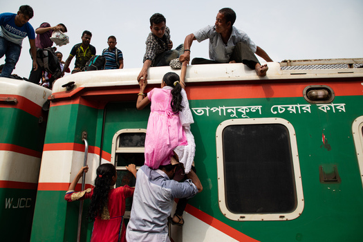 Dhaka Bangladesh 14 June 2018 View of people climbing onto the roof of a train at Airport Railway Station with men helping a young girl up while others wait to board. Dhaka Bangladesh 14 June 2018 View of people climbing onto the roof of a train at Airport Railway Station with men helping a young girl up while others wait to board.