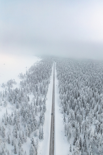 Aerial view of a straight road cutting through a dense snow covered pine forest near Yllas in the winter landscape of Kolari Lapland Finland. Aerial view of a straight road cutting through a dense snow covered pine forest near Yllas in the winter landscape of Kolari Lapland Finland.