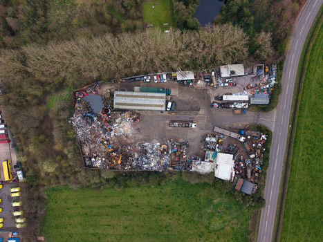 Aerial view of a scrap yard filled with metallic debris and colorful refuse near a road and a patch of trees Stafford England United Kingdom. Aerial view of a scrap yard filled with metallic debris and colorful refuse near a road and a patch of trees Stafford England United Kingdom.