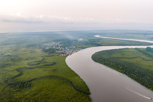 Aerial view of a winding river flowing through lush mangrove forests with a small town nestled on the bank and a boat leaving a wake in the water in Opobo Town Rivers Nigeria. Aerial view of a winding river flowing through lush mangrove forests with a small town nestled on the bank and a boat leaving a wake in the water in Opobo Town Rivers Nigeria.