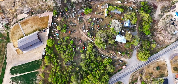 Aerial view of a junkyard dotted with colorful vehicles amidst lush greenery and buildings contrasting with the adjacent open field Palisade Colorado USA. Aerial view of a junkyard dotted with colorful vehicles amidst lush greenery and buildings contrasting with the adjacent open field Palisade Colorado USA.