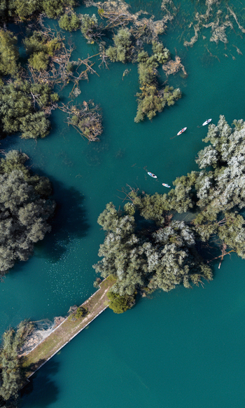 Aerial view of Lago di Barrea with paddleboarders gliding across turquoise water surrounded by lush green islands and trees in Province of L Aquila Abruzzo Italy.