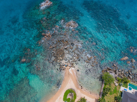 Aerial view of the turquoise ocean embracing the rocky shore with a glimpse of sandy beach and lush greenery Vista do Mar Mahe Island Seychelles. Aerial view of the turquoise ocean embracing the rocky shore with a glimpse of sandy beach and lush greenery Vista do Mar Mahe Island Seychelles.