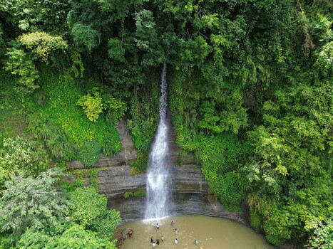 Aerial view of the waterfall surrounded by dense green forest and rocky cliffs with people swimming in the pool at the base in Sitakund Chittagong Division Bangladesh. Aerial view of the waterfall surrounded by dense green forest and rocky cliffs with people swimming in the pool at the base in Sitakund Chittagong Division Bangladesh.