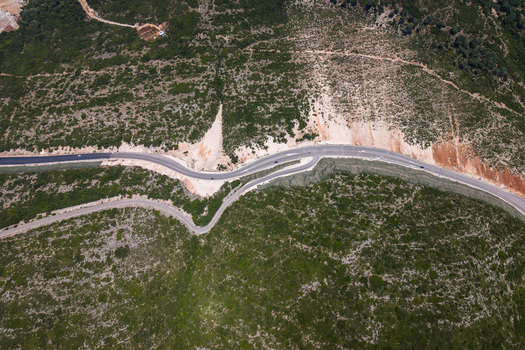 Aerial view of the winding asphalt road at Panorama Llogora passing through the green scrubland and rocky hillsides in Himare Qarku i Vlores Albania.
