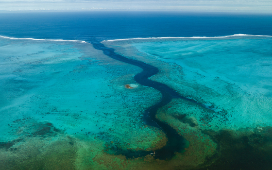 Aerial view of the deep blue pass meandering through the shallow turquoise waters contrasting with the vibrant coral reefs below Noumea South Province New Caledonia.