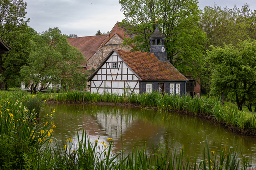 View of the Hennebergisches Museum Kloster Vessra featuring a half timbered house with a clock tower reflected in a pond with yellow irises Kloster Vessra Thuringen Germany. View of the Hennebergisches Museum Kloster Vessra featuring a half timbered house with a clock tower reflected in a pond with yellow irises Kloster Vessra Thuringen Germany.