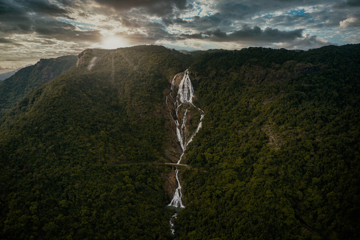 Aerial view of Dudhsagar Falls cascading through dense tropical forest under a dramatic cloudy sky at sunset Sonauli Goa India.