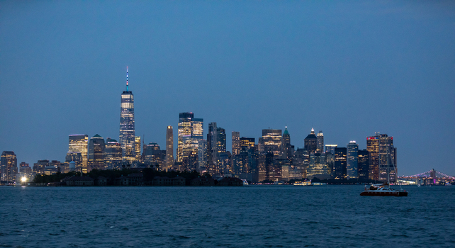 New York United States 21 July 2021 View of the New York City skyline at twilight with the One World Trade Center illuminated against the evening sky and a boat sailing on the water.