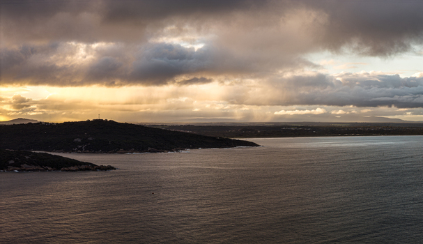 Aerial view of Quaranup Beach on the Vancouver Peninsula featuring dark storm clouds golden sunset light over the water and rugged coastline in Vancouver Peninsula Western Australia Australia.