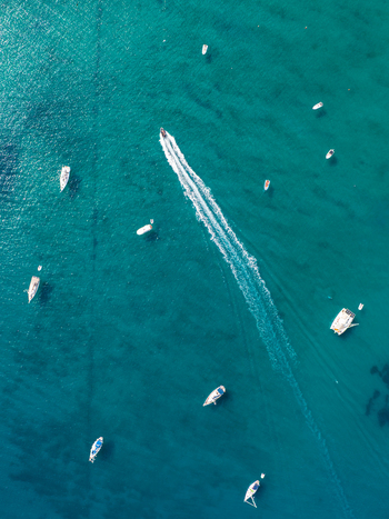 Aerial view of small boats and a motorboat creating a white wake in the clear turquoise waters of Lacona Tuscany Italy.