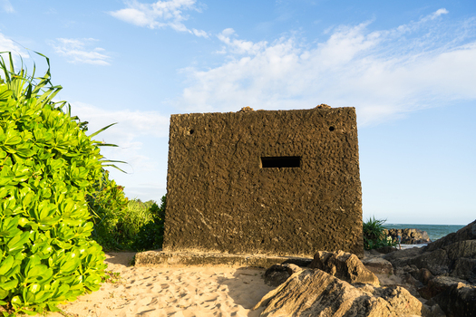View of a historic concrete bunker on a sandy beach surrounded by lush green vegetation and coastal rocks under a clear blue sky in Galle Southern Province Sri Lanka.