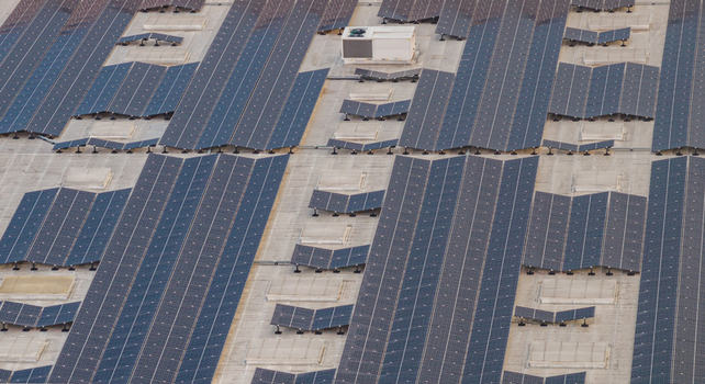 Aerial view of a large industrial rooftop covered with geometric rows of photovoltaic solar panels and HVAC equipment in Alixan Auvergne Rhone Alpes France.