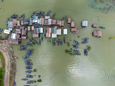 Aerial view of Kalabagi village with traditional thatched houses and numerous blue fishing boats moored in the water Khulna District Khulna Division Bangladesh.