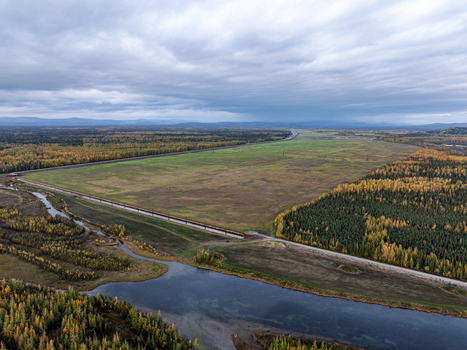 Aerial view of the Moose Creek landscape featuring a long pipeline crossing open fields winding river and dense autumn forest in Moose Creek Alaska United States.