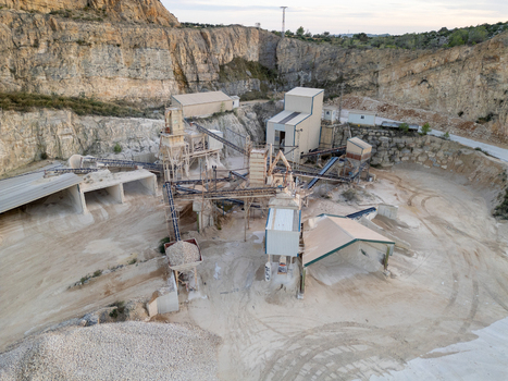 Aerial view of the stone quarry featuring industrial processing machinery conveyor belts and gravel piles set against a rocky cliff face in Teulada Valencian Community Spain.