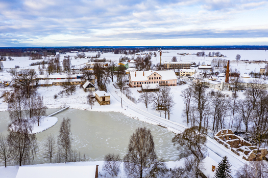 Aerial view of a frozen pond and a small island with trees surrounded by snow covered buildings and bare winter trees in the rural landscape of Latvia. Aerial view of a frozen pond and a small island with trees surrounded by snow covered buildings and bare winter trees in the rural landscape of Latvia.