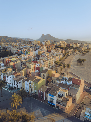 Aerial view of colorful houses along the coastline with a sandy beach and mountains under a clear sky in La Vila Joiosa Valencian Community Spain. Aerial view of colorful houses along the coastline with a sandy beach and mountains under a clear sky in La Vila Joiosa Valencian Community Spain.