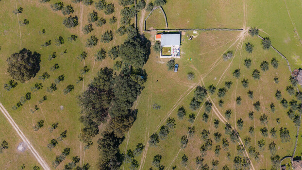 Aerial view of a solitary building with a red roof stands amidst a vibrant green field dotted with trees and winding dirt paths Navas del Madrono Extremadura Spain.