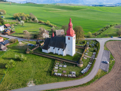 Aerial view of the historic Church of Saint Ladislaus with its red tower and stone wall enclosure overlooking green meadows and hills in Liptovske Matiasovce Zilina Region Slovakia.