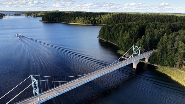 Aerial view of Potkusalmen silta Bridge spanning the deep blue lake surrounded by dense pine forests under a clear sky with a boat leaving a wake in Savonlinna Etela Savo Finland. Aerial view of Potkusalmen silta Bridge spanning the deep blue lake surrounded by dense pine forests under a clear sky with a boat leaving a wake in Savonlinna Etela Savo Finland.