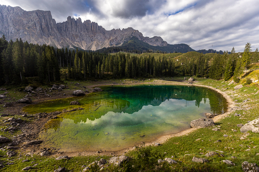 View of the emerald waters of Karersee reflecting the jagged peaks of the Latemar mountain range and surrounding pine forest in Welschnofen Trentino Alto Adige Italy.