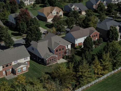 Aerial view of a suburban residential neighborhood featuring detached houses with brick and siding facades manicured lawns mature trees and a white fence in Mason Ohio United States.
