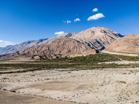 Aerial view of the rugged mountain landscape of Ladakh with a strip of green vegetation and dry desert terrain under a clear blue sky in Ladakh India. Aerial view of the rugged mountain landscape of Ladakh with a strip of green vegetation and dry desert terrain under a clear blue sky in Ladakh India.