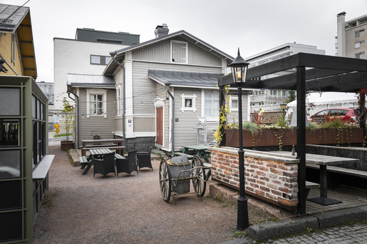 View of a cozy outdoor courtyard with a wooden house tables chairs a vintage cart and a brick walled seating area in Jyvaskyla Central Finland Finland.