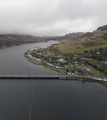 Aerial view of the village of Dornie and the A87 bridge crossing Loch Long under a misty sky with green hills Dornie Scotland United Kingdom.