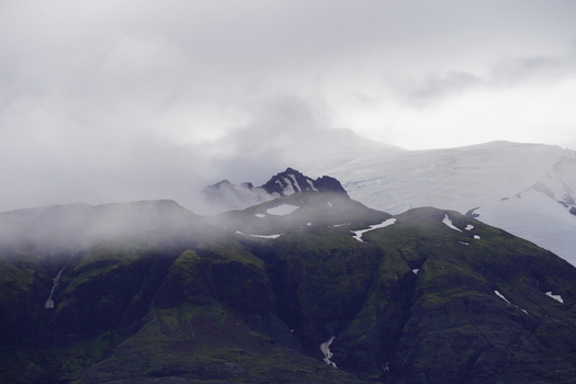 View of the snow capped peaks of Skaftafell partially obscured by thick clouds and mist over lush green mountain slopes in Skaftafell Hornafjordur Iceland. View of the snow capped peaks of Skaftafell partially obscured by thick clouds and mist over lush green mountain slopes in Skaftafell Hornafjordur Iceland.