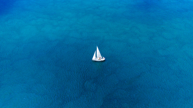 Aerial view of a white sailboat sailing across the deep blue waters of the Danube river with gentle ripples on the surface Novi Sad Vojvodina Serbia.