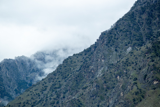 View of steep rocky mountain slopes covered with sparse green vegetation and shrouded in thick white mist under a cloudy sky Chilas Gilgit Pakistan. View of steep rocky mountain slopes covered with sparse green vegetation and shrouded in thick white mist under a cloudy sky Chilas Gilgit Pakistan.