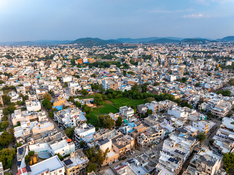 Aerial view of the sprawling cityscape of Udaipur with dense residential buildings green patches and distant hills under a clear blue sky in Udaipur Rajasthan India. Aerial view of the sprawling cityscape of Udaipur with dense residential buildings green patches and distant hills under a clear blue sky in Udaipur Rajasthan India.