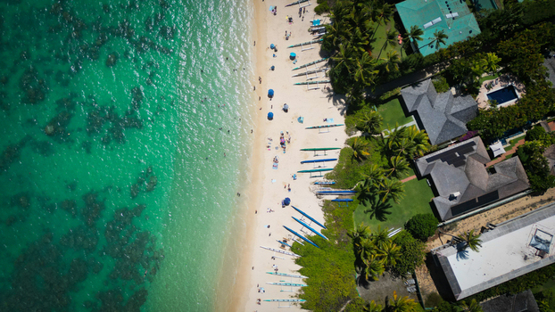 Aerial view of the turquoise ocean meeting the sandy beach with canoes lined up adjacent to houses and palm trees Kailua Hawaii United States. Aerial view of the turquoise ocean meeting the sandy beach with canoes lined up adjacent to houses and palm trees Kailua Hawaii United States.